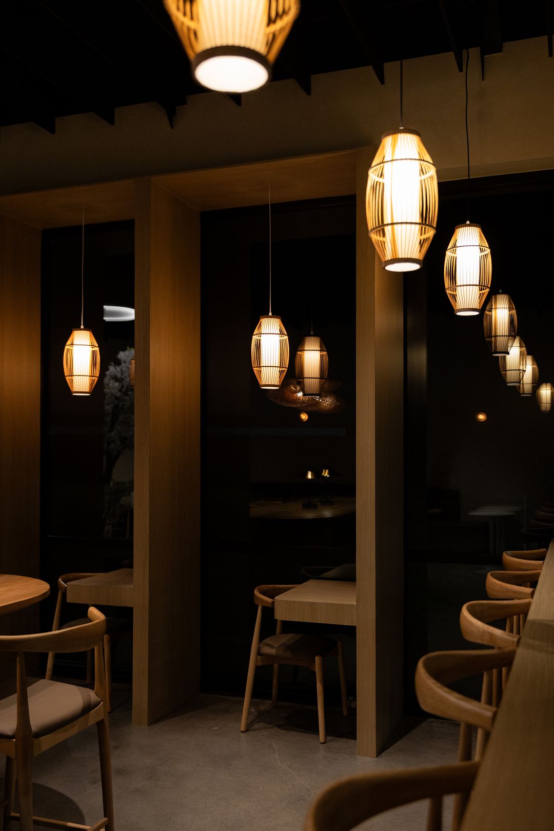 Inside Fresso Cafe at night: woven lanterns glowing over oak booths and curved wooden chairs